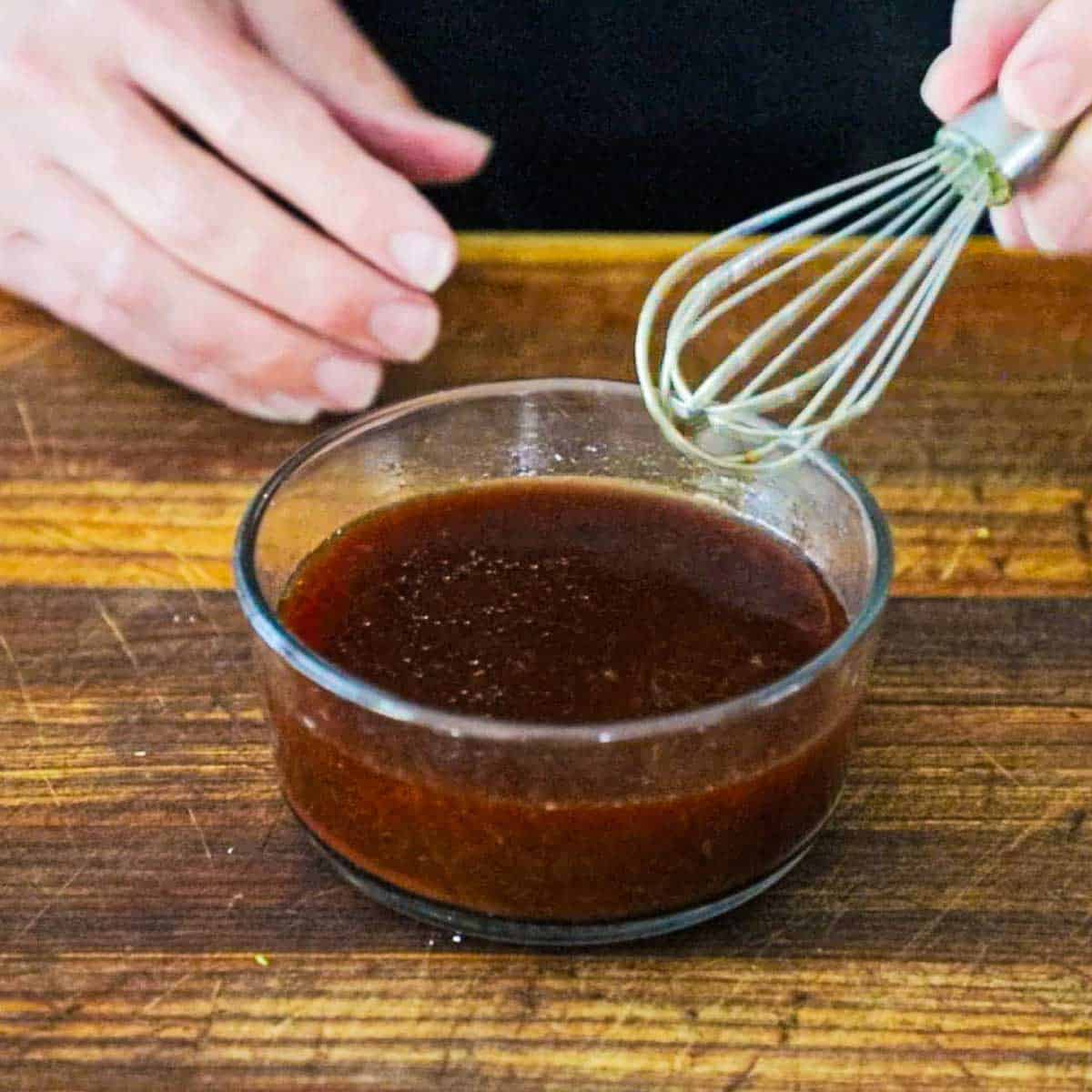 A person using a small whisk to combine the ingredients together for a sweet and sour sauce in a small glass bowl.