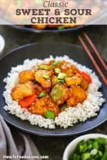 A straight-on view of a black plate filled with a bed of white steamed rice topped with sweet and sour chicken stir-fry.