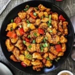 An overhead view of a large black dinner plate filled with Classic Sweet and Sour Chicken Stir-Fry with a bowl of cooked white rice nearby.
