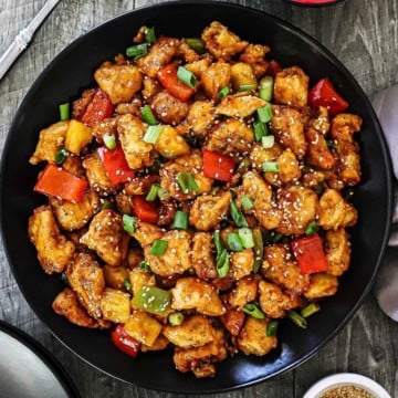 An overhead view of a large black dinner plate filled with Classic Sweet and Sour Chicken Stir-Fry with a bowl of cooked white rice nearby.