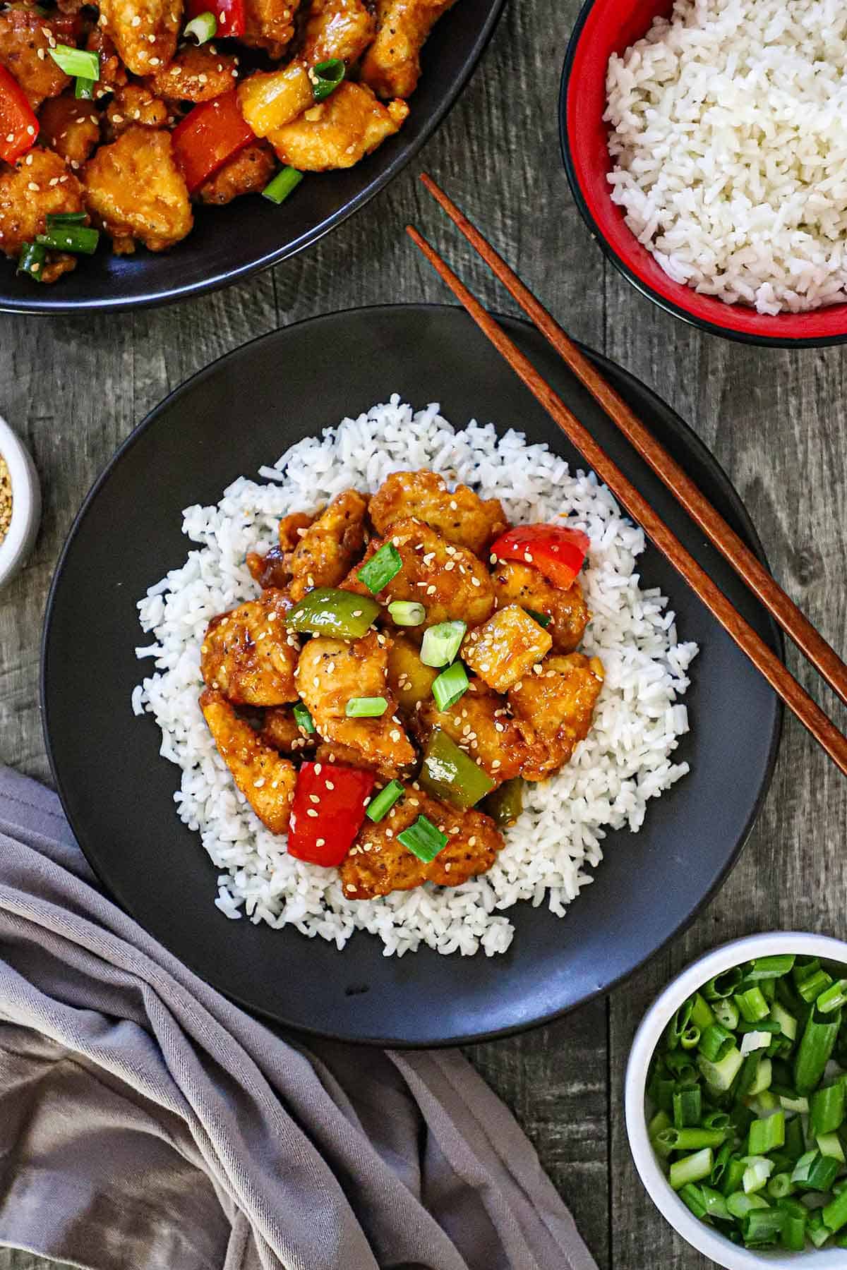 An overhead view of a black dinner plate filled with Classic Sweet and Sour Chicken Stir-Fry served over a bed of white rice.