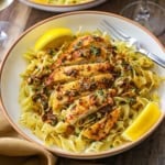 An overhead view of a shallow pasta bowl filled with a serving of Cowboy Butter Chicken with Egg Noodles with two lemon wedges on each side of the dish.