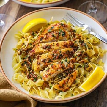 An overhead view of a shallow pasta bowl filled with a serving of Cowboy Butter Chicken with Egg Noodles with two lemon wedges on each side of the dish.