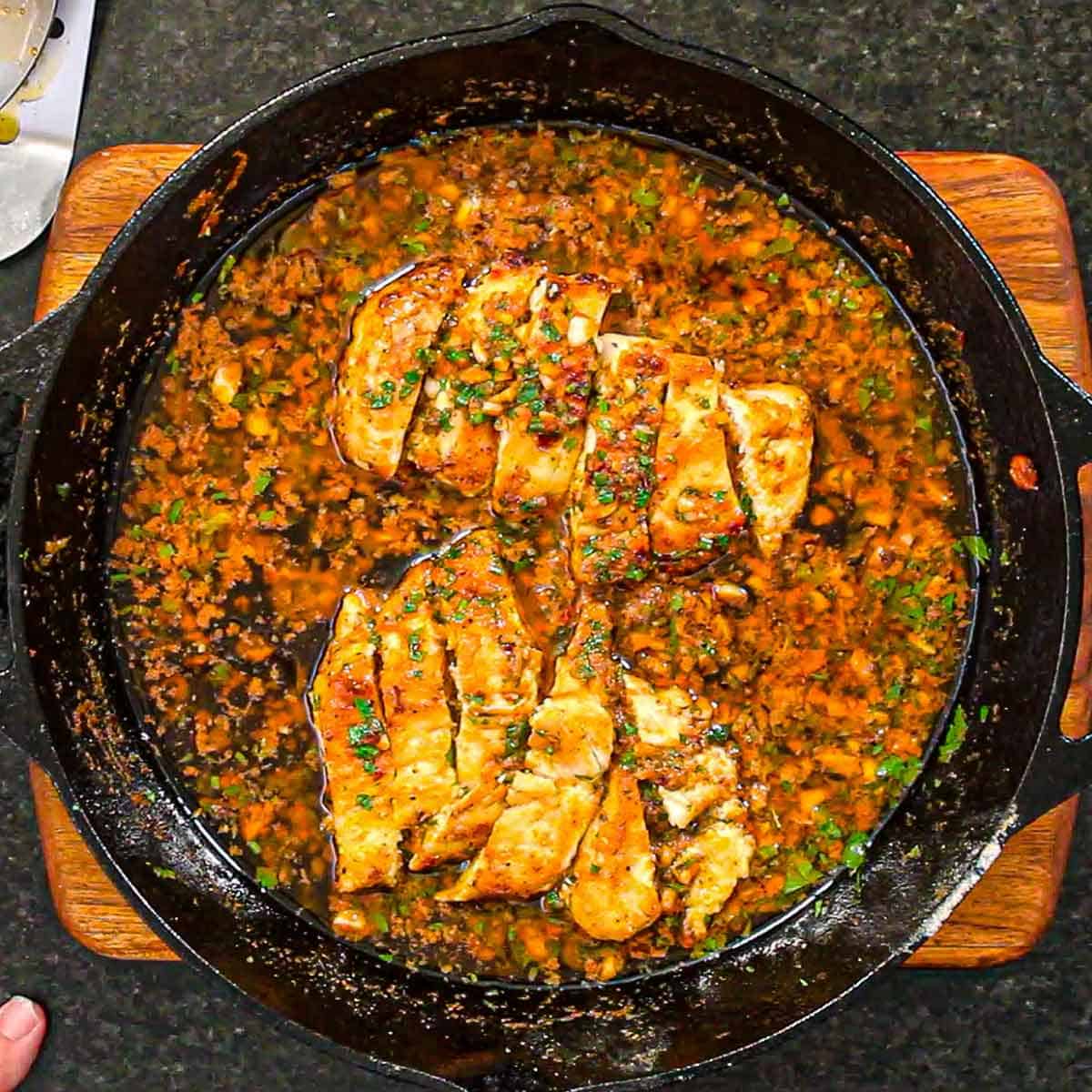 An overhead view of strips of seared chicken breasts resting in a Cowboy butter sauce in a large cast-iron skillet.