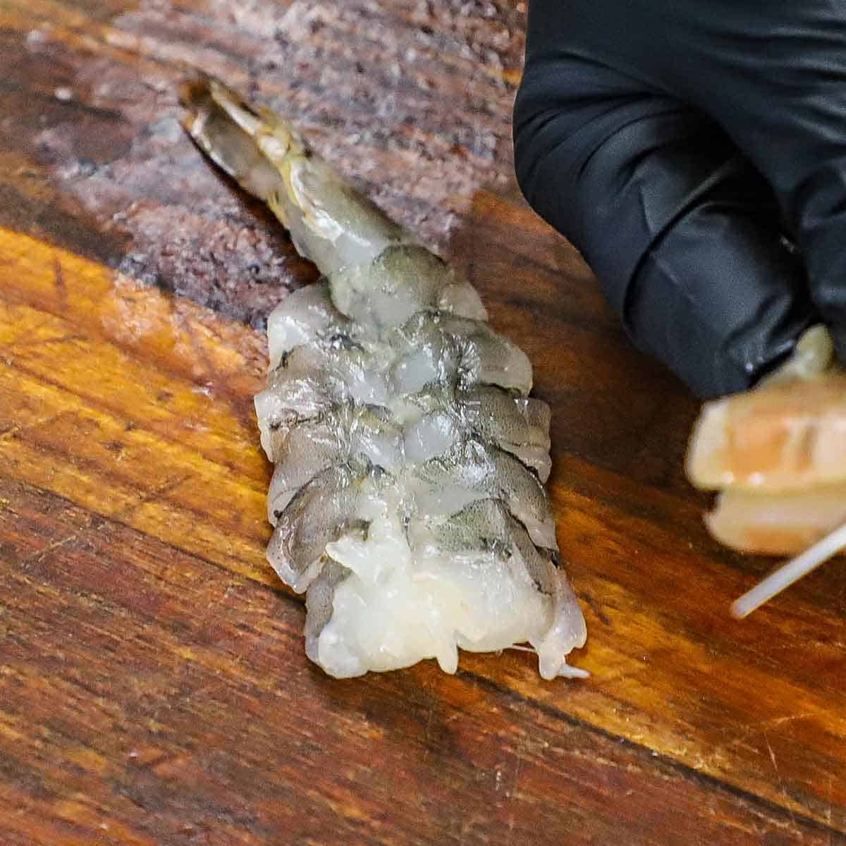 An uncooked extra-large shrimp that has been butterflied open and is resting on a large wooden cutting board.
