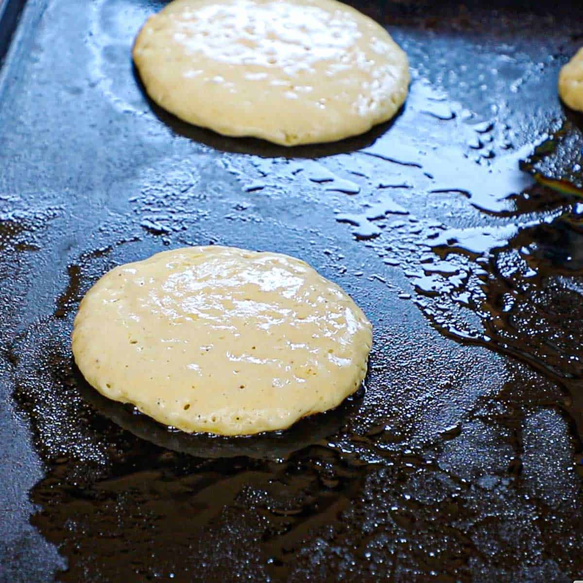 Two buttermilk pancakes being cooked on a large outdoor griddle in a hot oil and melted butter.