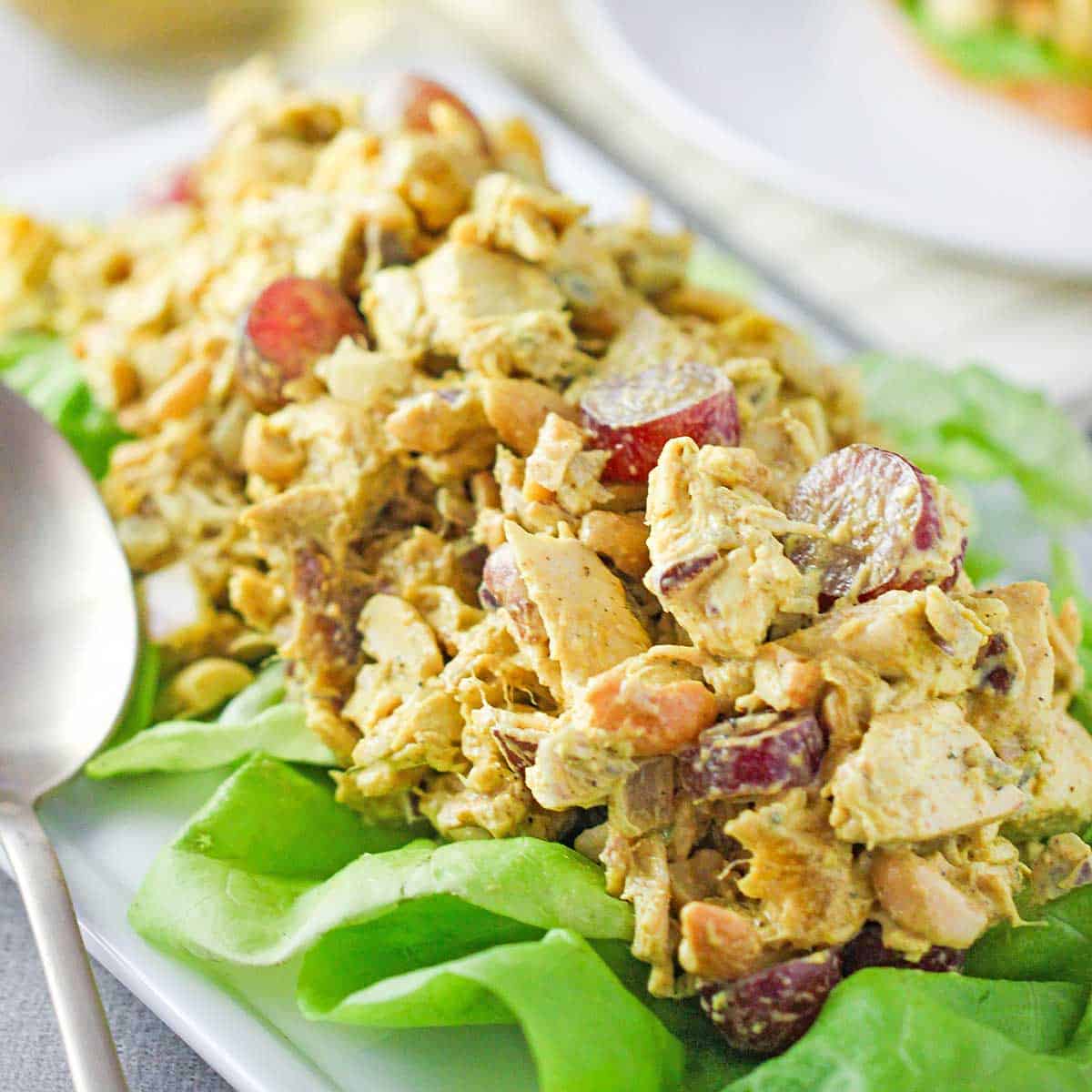 A mound of curried chicken salad over a bed of green leaf lettuce on a white rectangular platter.