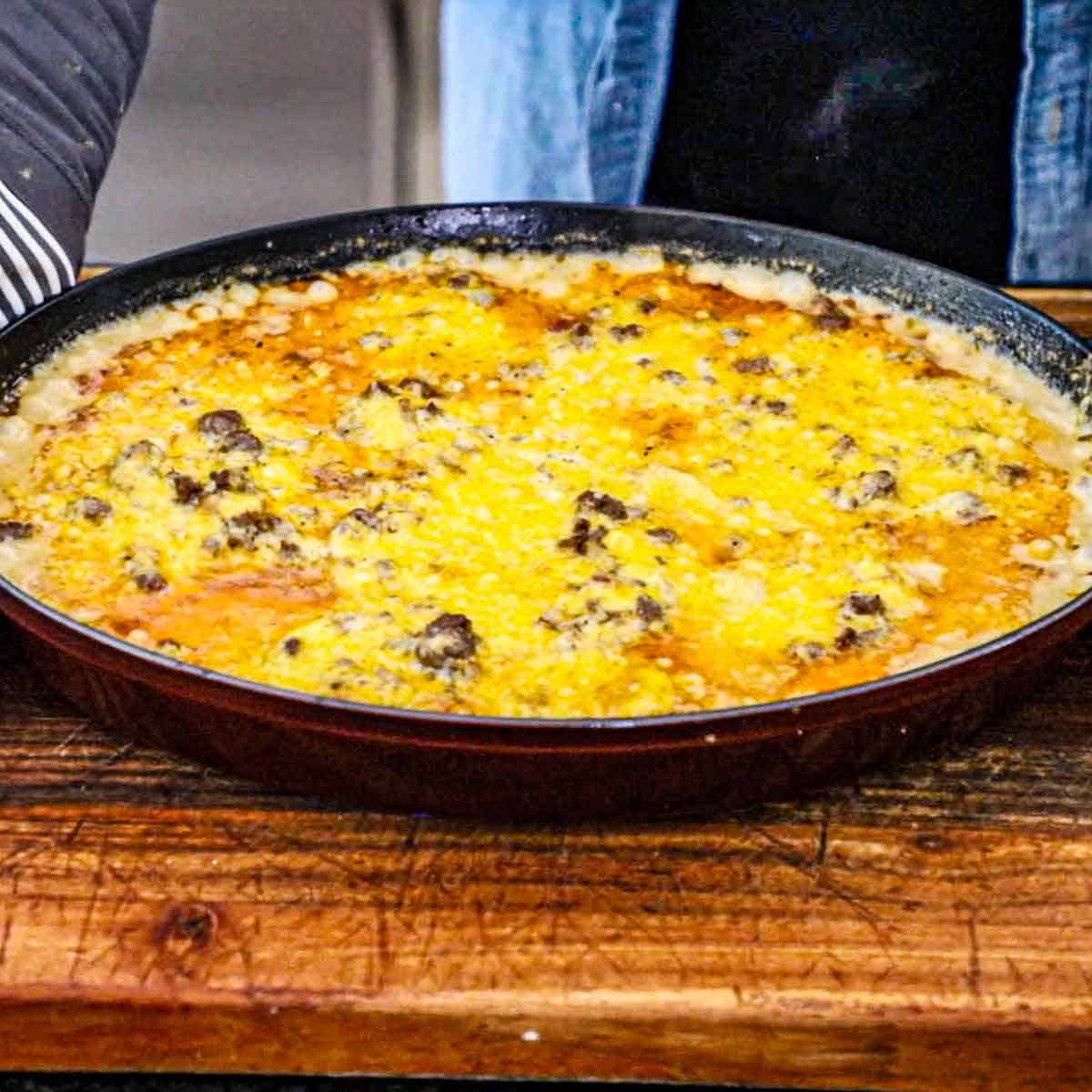 A large oval casserole dish filled with a freshly baked hamburger potato casserole resting on a wooden cutting board.
