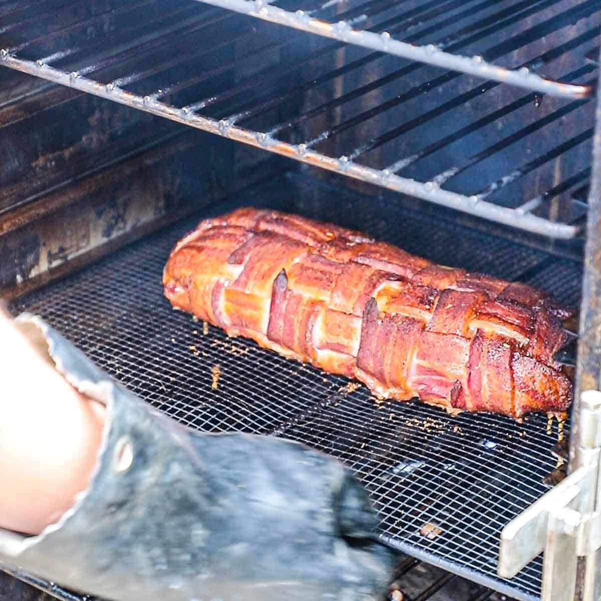 A person wearing heat-resistant gloves pulling a wire rack that is holding a smoked Western omelette Fatty from an electric smoker.