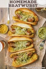 An overhead view of four homemade bratwurst links that have been cooked, seared, and placed in a bun with brown mustard and sauerkraut.