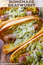 An overhead view of four homemade bratwurst links that have been cooked, seared, and placed in a bun with brown mustard and sauerkraut.