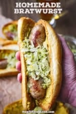A person holding a homemade bratwurst sausage in a toasted roll with brown mustard and topped with homemade sauerkraut.