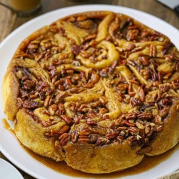 A straight-on view of a Caramel Pecan Sticky Buns in a circular formation resting on a white round serving platter with caramel sauce at the bottom of the pastry.