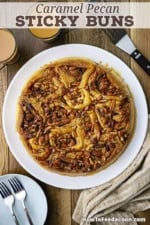 An overhead view of a circular formation of Caramel Pecan Sticky Buns resting on a white round serving platter.