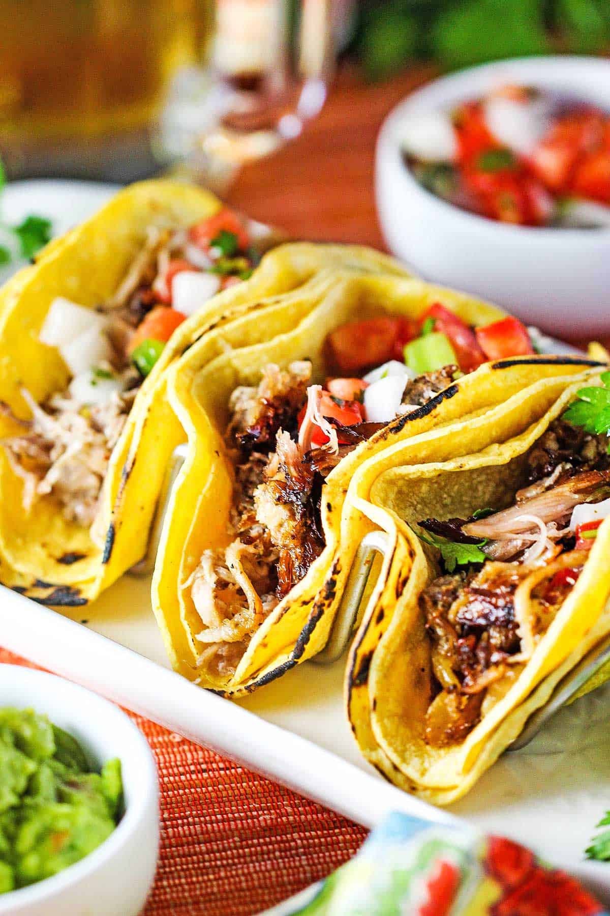 A close-up view of three double-stacked slow cooker carnitas tacos resting upright on a metal taco holder.