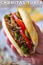 A person holding a homemade carnitas torta sandwich in the palm of his hand with the shredded pork filling and juicy vegetables clearly visible.