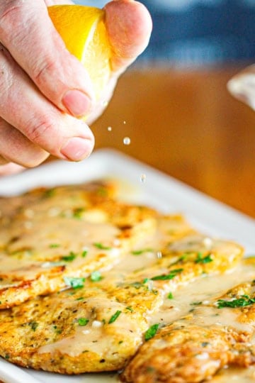A lemon wedge being squeezed onto a platter of chicken francese.