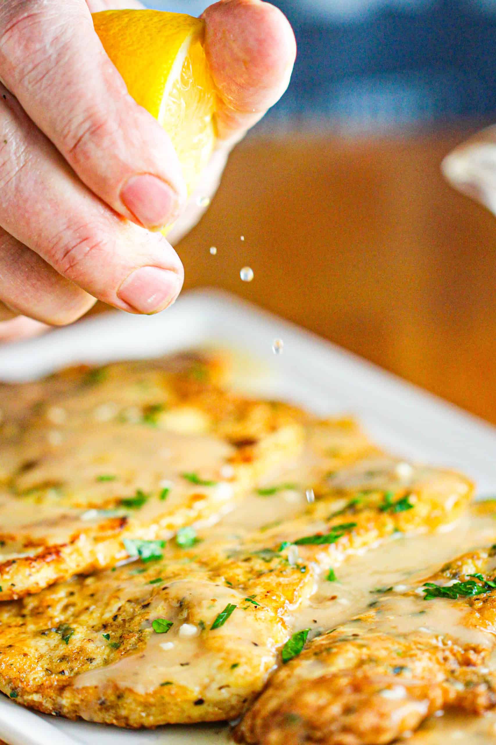 A lemon wedge being squeezed onto a platter of chicken francese.