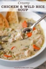 A person holding a spoonful of Creamy Chicken and Wile Rice Soup over a bowl of te same.