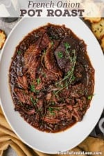 An overhead view a large oval deep platter filled with a French Onion Pot Roast that is shredded and garnished with two twigs of thyme.
