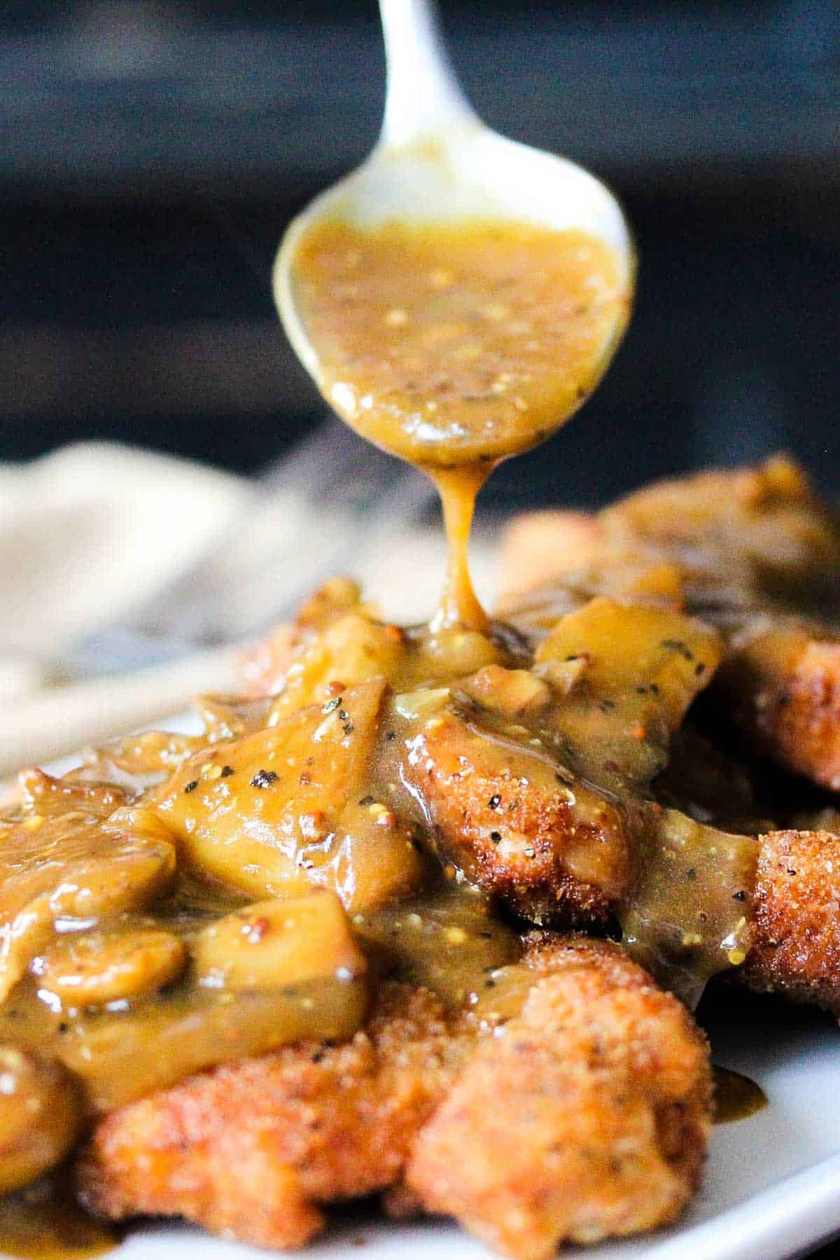 A person using a large spoon to drizzle a mushroom sauce over a platter of German Pork Schnitzel.