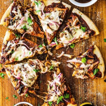 An overhead view of a Grilled Pulled Pork Pizza that has been cut into slices on a wooden cutting board sprinkled with cornmeal.