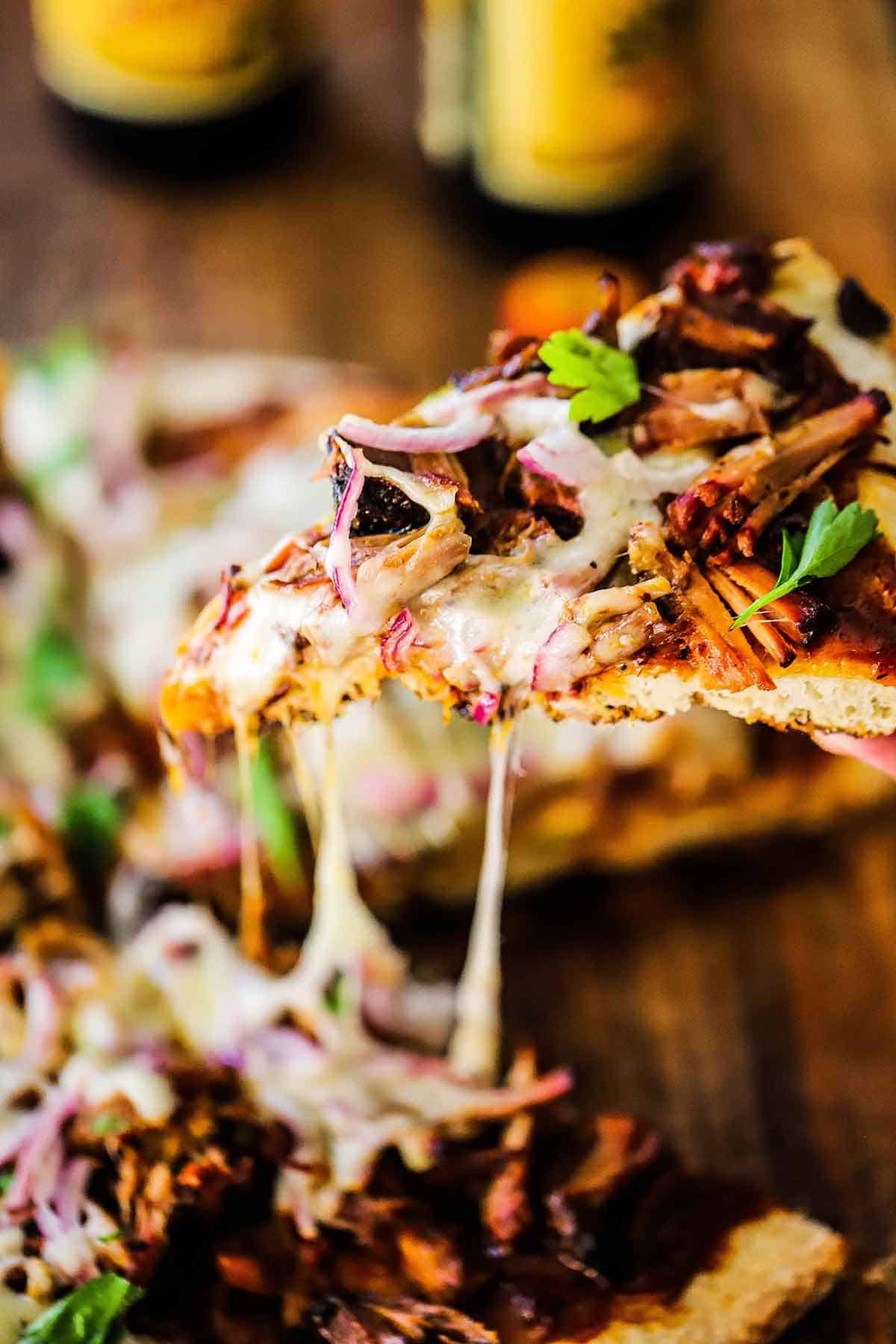 A person holding a slice of Grilled Pulled Pork Pizza.