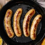 An overhead view of four links of seared homemade bratwurst in a black cast-iron skillet.