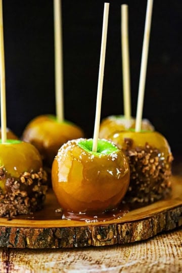A straight-on view of Honey Caramel Apples resting on a plate that is a slice of a tree trunk.