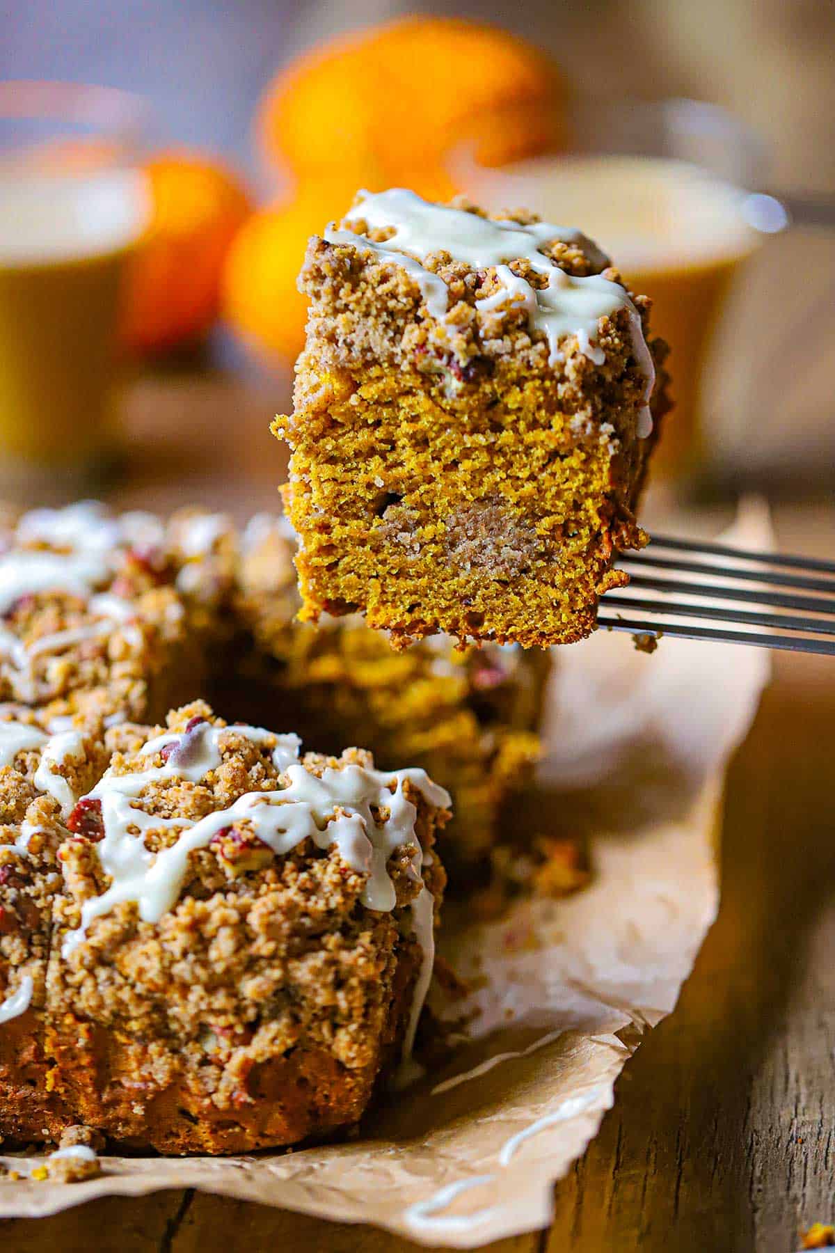 A person using a metal spatula to raise a square piece of Pumpkin Spice Coffee Cake from other slices of the cake that are all resting on brown paper.