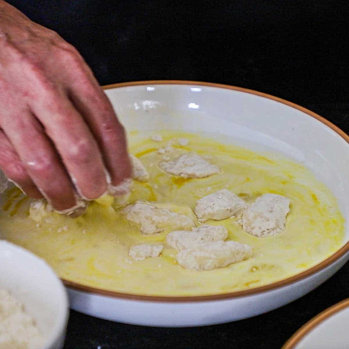 A person using his hands to toss cheese curds that have been coated with flour in an egg and buttermilk bath in a shallow bowl.