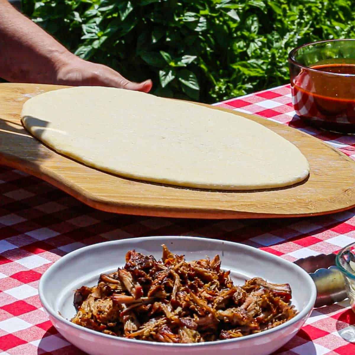 A person holding a wooden pizza peel with a large round pizza dough on top of it.