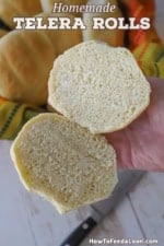 A person holding split open homemade telera roll in the palm of his hand revealing the soft crumb interior of the bread.