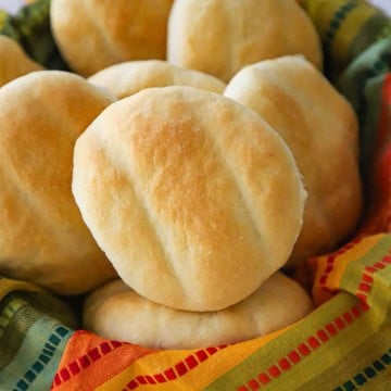 A straight-on view of a bread basket lined with a festive linen and filled with homemade telera rolls.