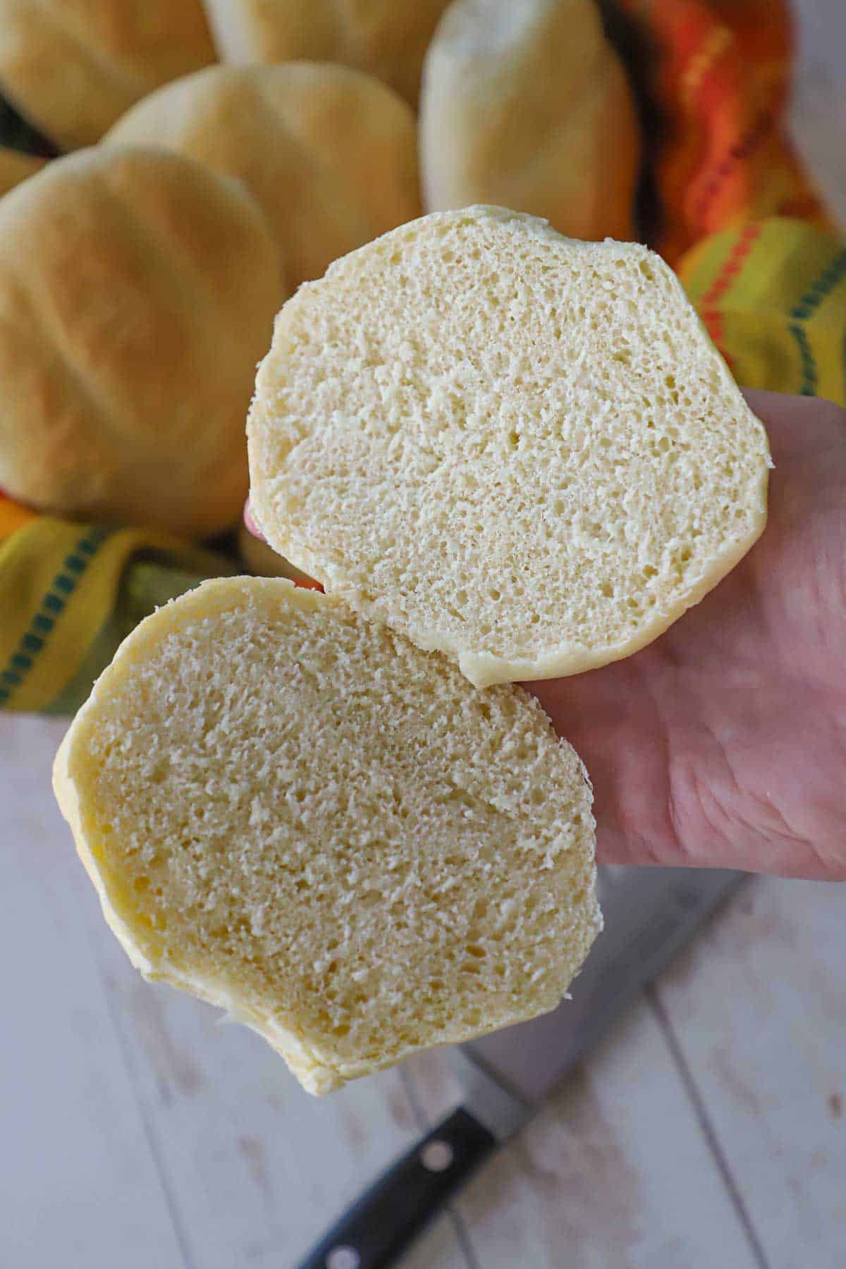 A person holding split open homemade telera roll in the palm of his hand revealing the soft crumb interior of the bread.