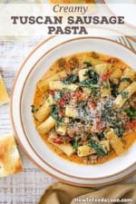 An overhead view of a shallow bowl filled with a serving of Tuscan Sausage Pasta loaded with spinach, sun-dried tomatoes, and crumbled sausage topped with grated Parmesan cheese.