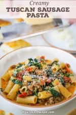 A close-up view of a shallow bowl filled with a serving of Tuscan Sausage Pasta loaded with spinach, sun-dried tomatoes, and crumbled sausage topped with grated Parmesan cheese.