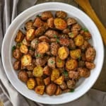 An overhead view of a shallow white serving bowl filled with a mound of Crispy Air-Fryer Baby Potatoes garnished with coarse sea salt and chopped parsley.