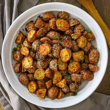 An overhead view of a shallow white serving bowl filled with a mound of Crispy Air-Fryer Baby Potatoes garnished with coarse sea salt and chopped parsley.