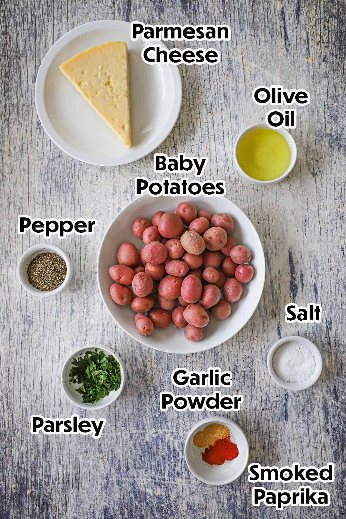 An arrangement of ingredients for Crispy Air-Fryer Baby Potatoes on a grey wooden background including baby red potatoes, olive oil, Parmesan, fresh chopped parsley, and seasonings.