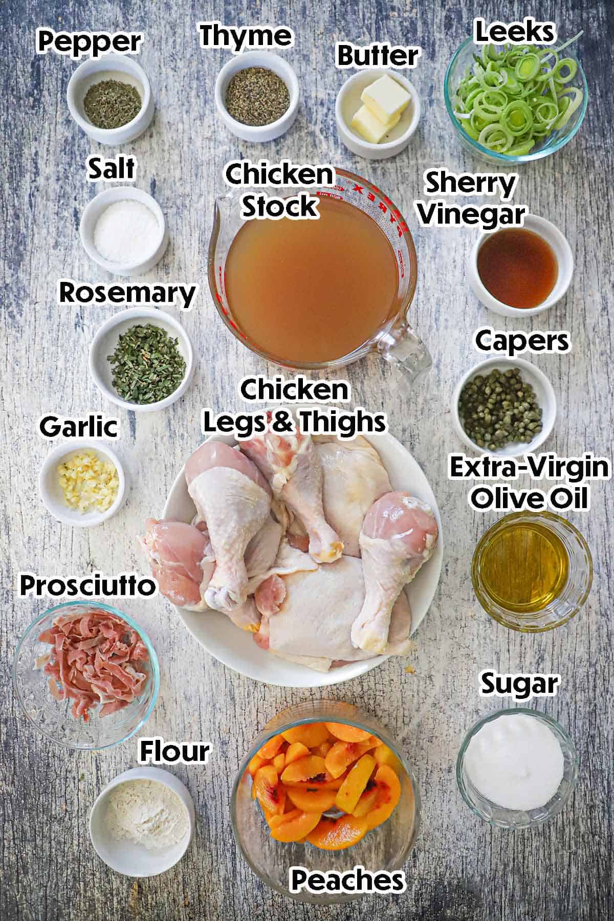 An arrangement of ingredients for Braised Chicken and Peaches on a grey wooden background including chicken legs and thighs, fresh slices of peaches, prosciutto, leeks, garlic, capers, chicken stock, spices, and seasonings.