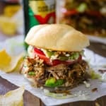 A straight-on view an overflowing carnitas torta packed with layers of refried beans, avocado, carnitas, tomatoes, jalapeños, Cotija cheese, all on a homemade telera bun.
