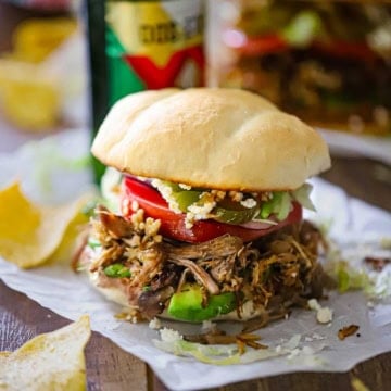 A straight-on view an overflowing carnitas torta packed with layers of refried beans, avocado, carnitas, tomatoes, jalapeños, Cotija cheese, all on a homemade telera bun.