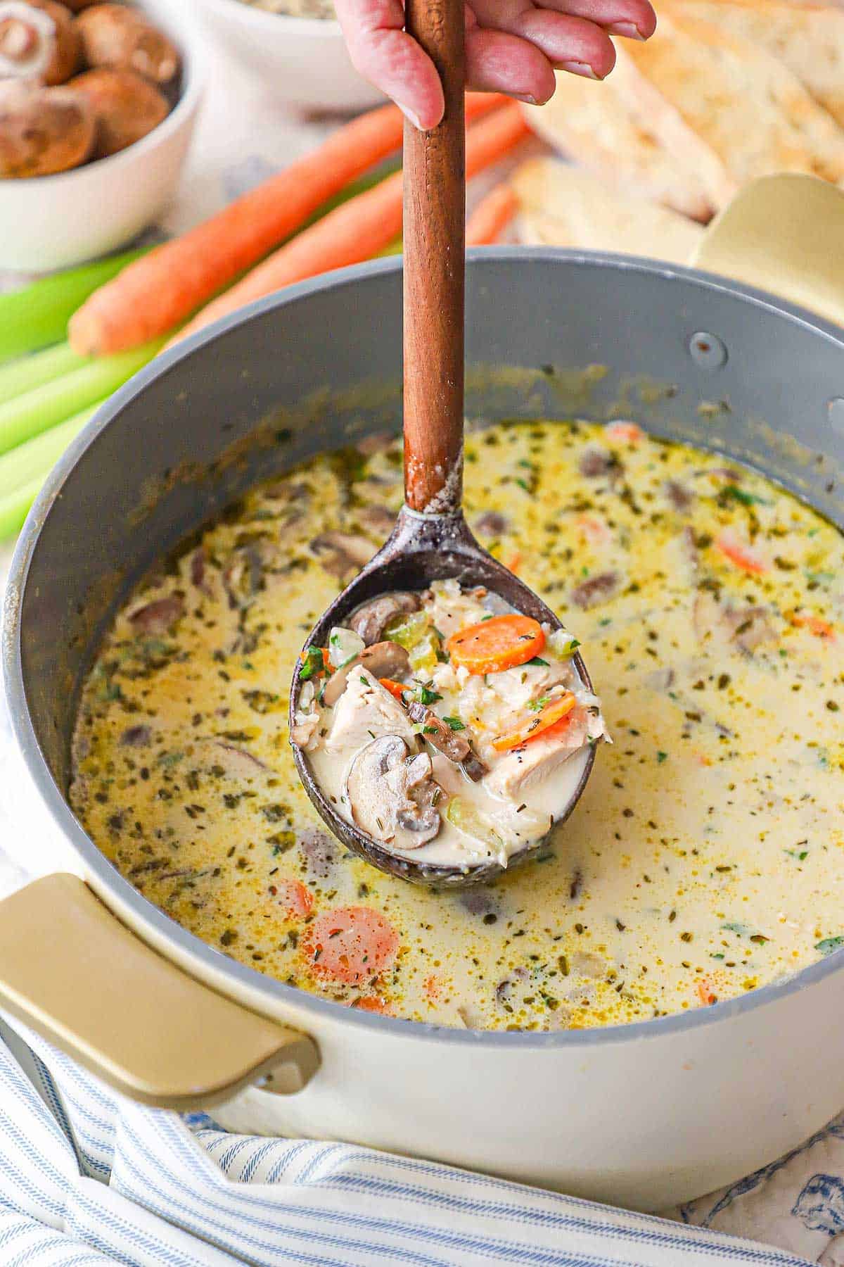 A person raising a wooden ladle from a pot filled with Creamy Chicken and Wild Rice Soup with the ladle also filled with the soup.