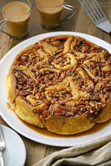 A straight-on view of a Caramel Pecan Sticky Buns in a circular formation resting on a white round serving platter with caramel sauce at the bottom of the pastry.