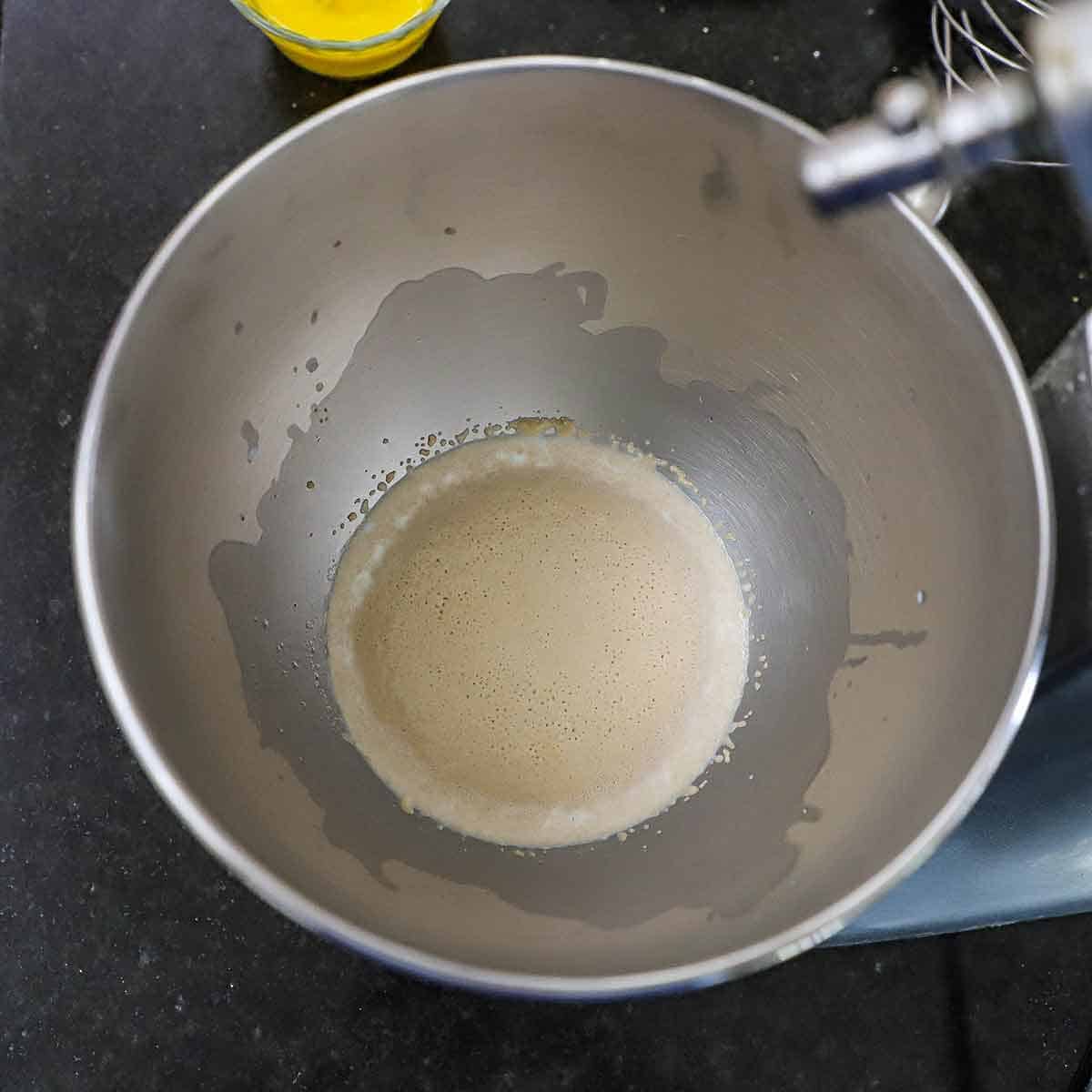 An overhead view of yeast that has been activated in warm milk in the bowl of a stand mixer.
