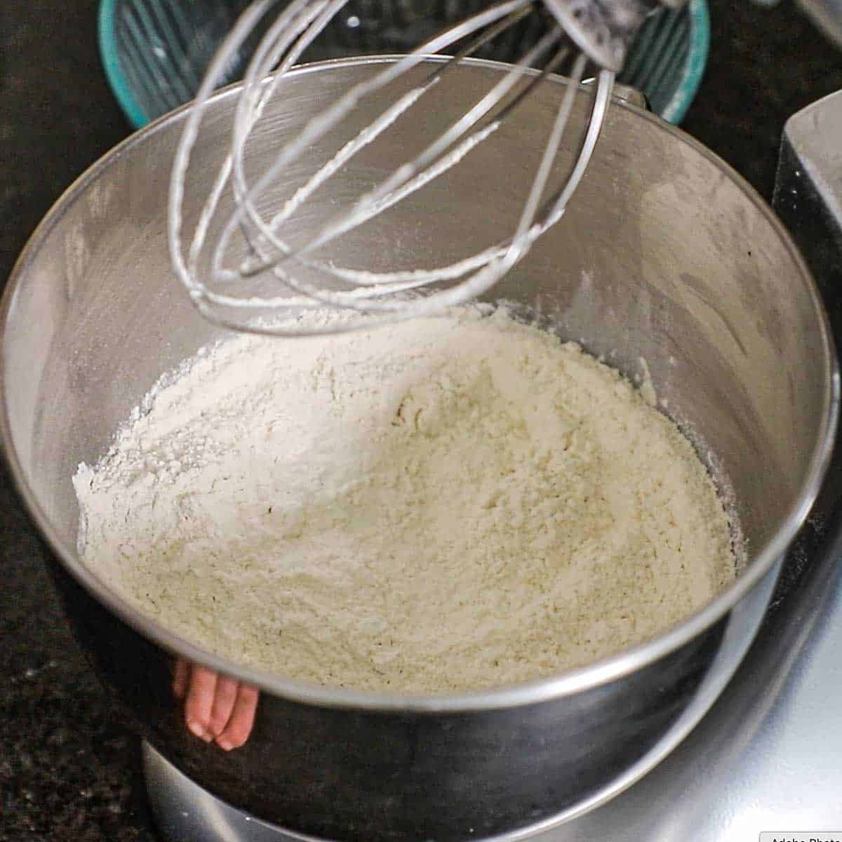 A view into the bowl of a stand mixer with flour in it that has been whisked with yeast, sugar, and salt.