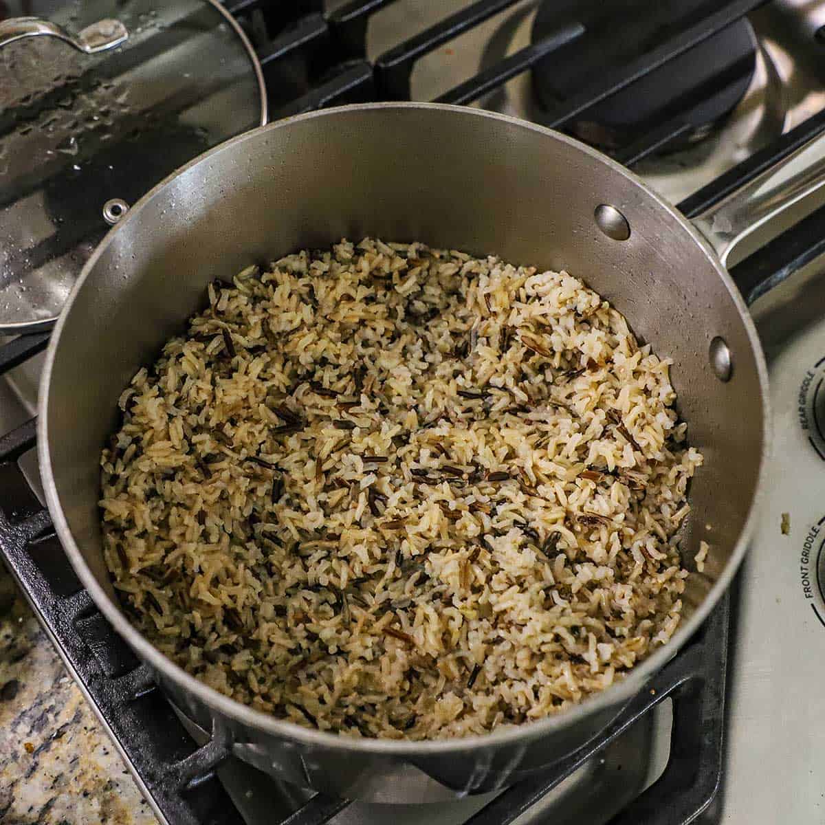 An overhead view of a medium-sized saucepan that is filled with fully cooked a wild rice and long grain rice blend on a gas stove.