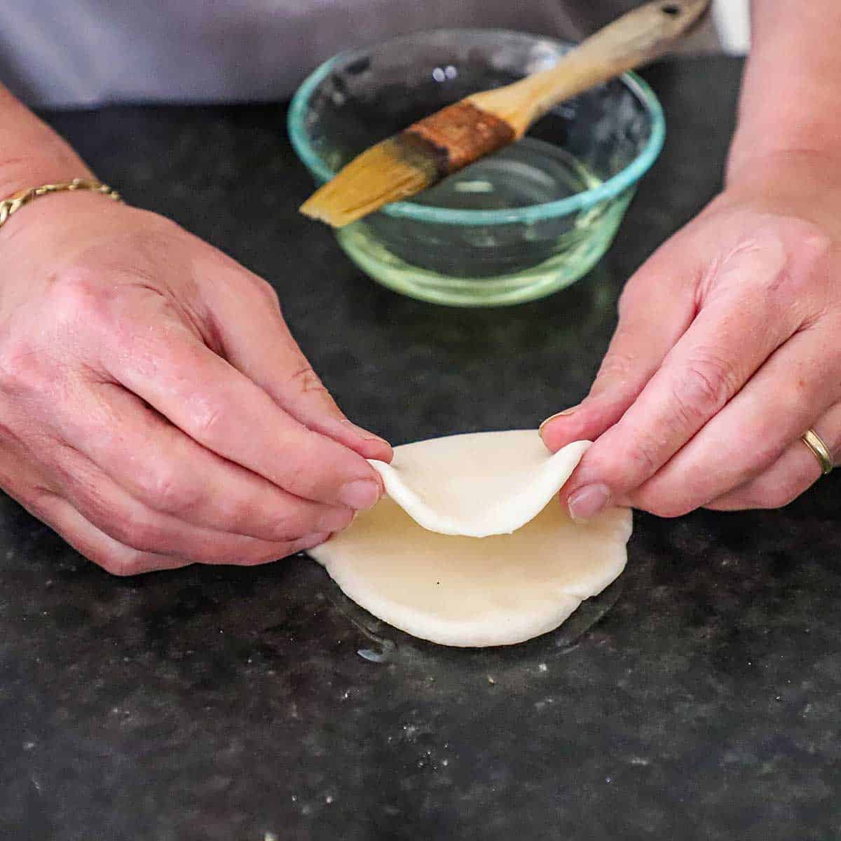 A person folding over an oval piece of bao bun dough that has been lightly brushed with vegetable oil.