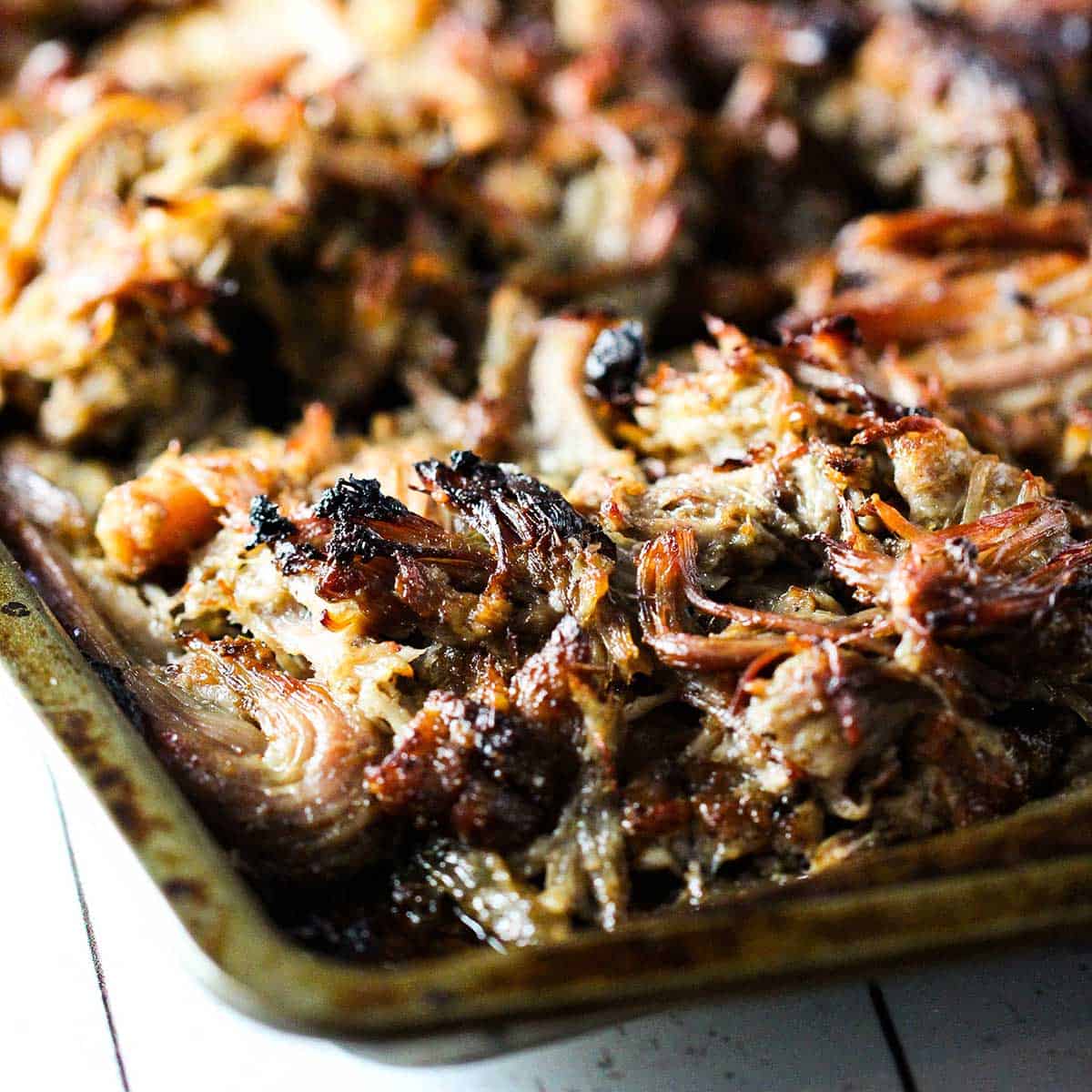 Shredded pork carnitas on a metal baking sheet that has been lightly charred under a broiler.